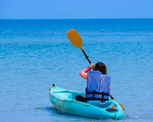 Aerial view of a woman kayaking in the blue sea and clear water. You can see corals under the sea.